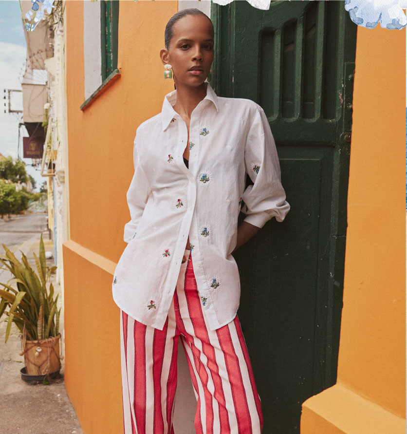 Modelo con camisa blanca bordada y pantalón a rayas rojas